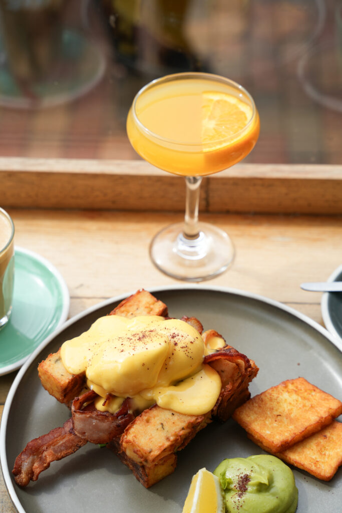 A bright photo of a Bottomless Brunch with a delicious looking breakfast meal, a latte and mimosa.