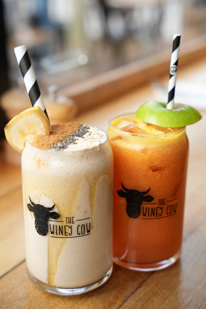 A photo of a delicious banana smoothie and a colourful juice sitting side-by-side on a wooden table.