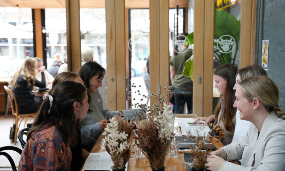 A photo of 6 happy ladies sitting down at a table chatting and laughing together.