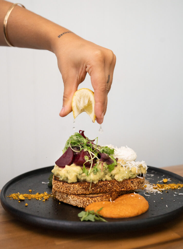 A photo of a lemon being squeezed over a smashed avocado dish.