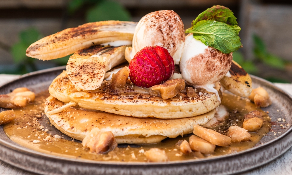 A stack of two golden pancakes with caramel sauce, topped with scoops of ice cream and caramelised banana.