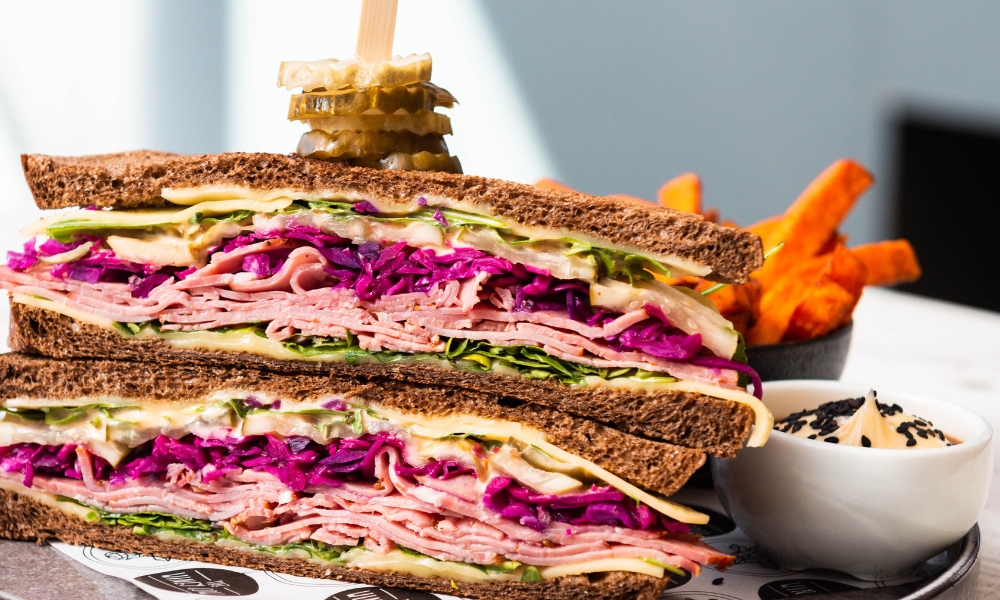 A close up image of a delicious Rueben sandwich, with layers of pastrami, pickles and slaw.