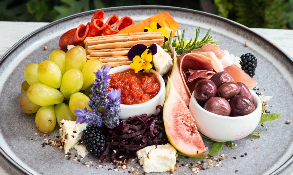 A photo of a cheese platter with assorted fruits, cheeses, crackers and dips.