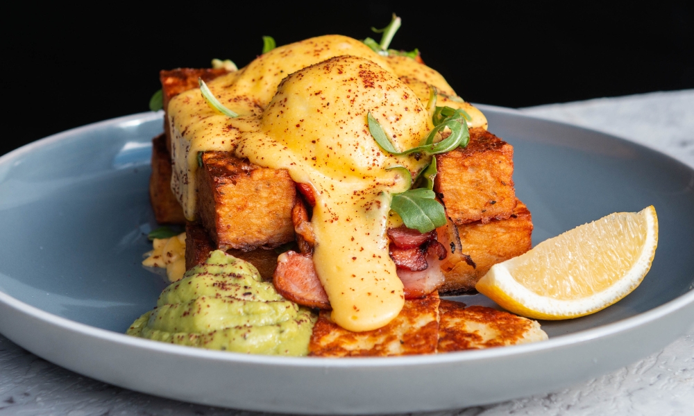 A photo of a breakfast meal, including potato rostis with poached eggs, hollandaise, avocado and halloumi.