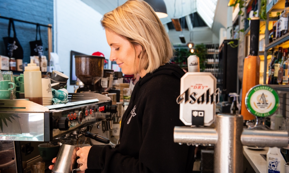 Photo of a staff member wearing black and steaming milk for a coffee.