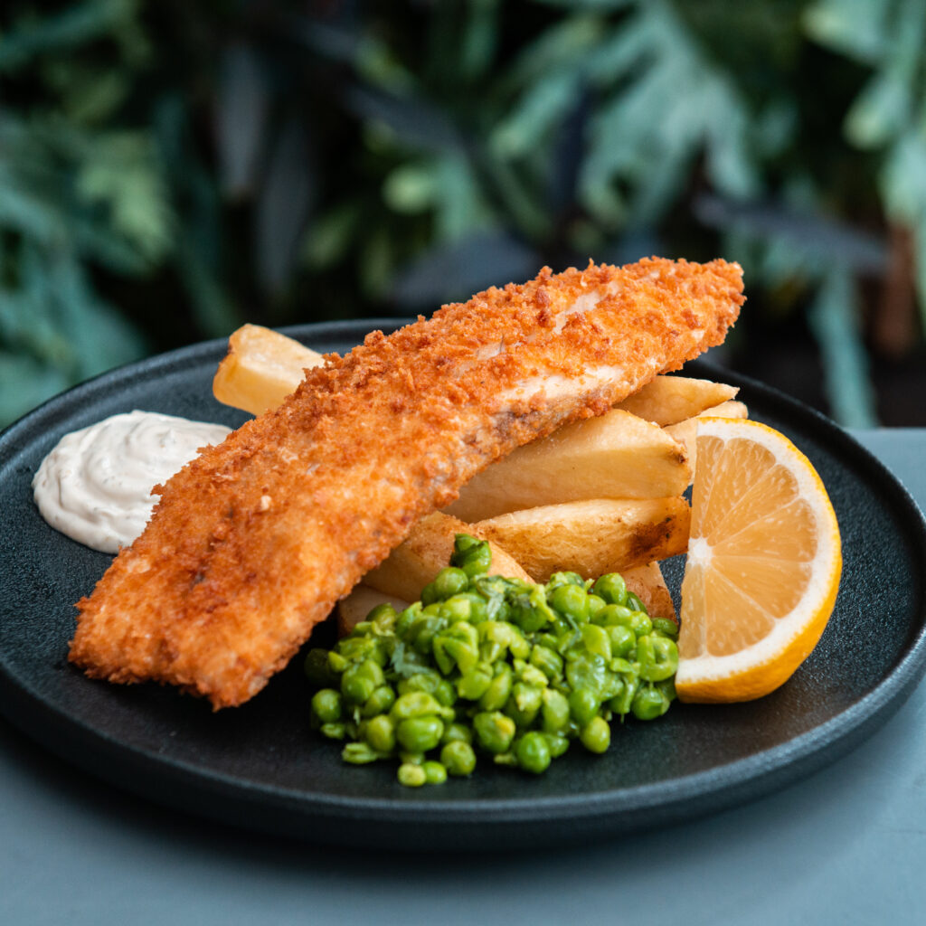A photo of crumbed fish & chips with peas and a lemon wedge.