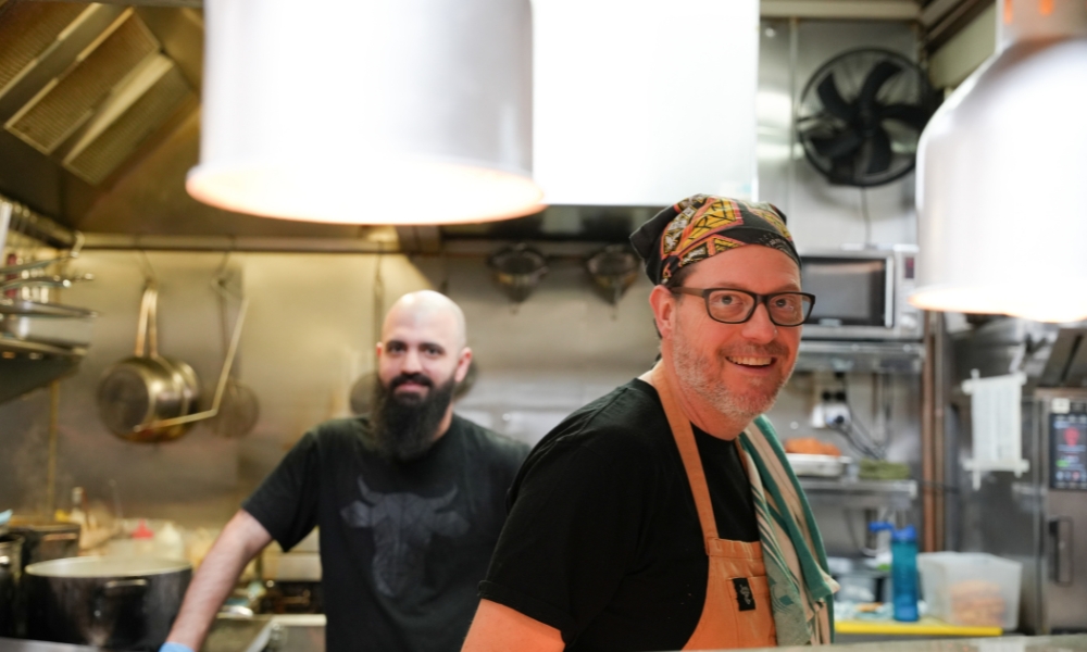 A photo of two chefs at The Winey Cow smiling at the camera whilst standing in the kitchen.