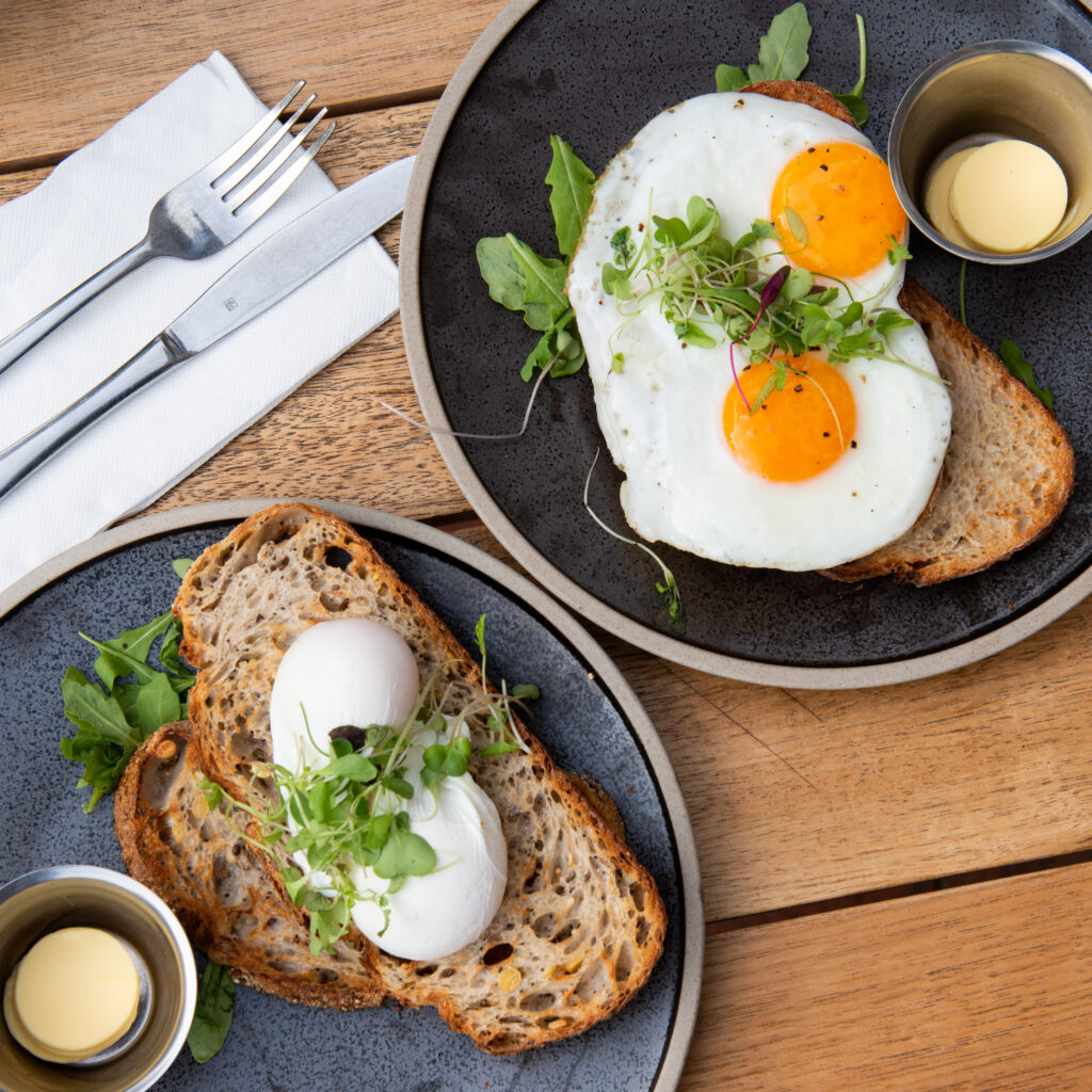 A photo of two servings of eggs on toast, poached eggs and fried eggs on a wooden table.