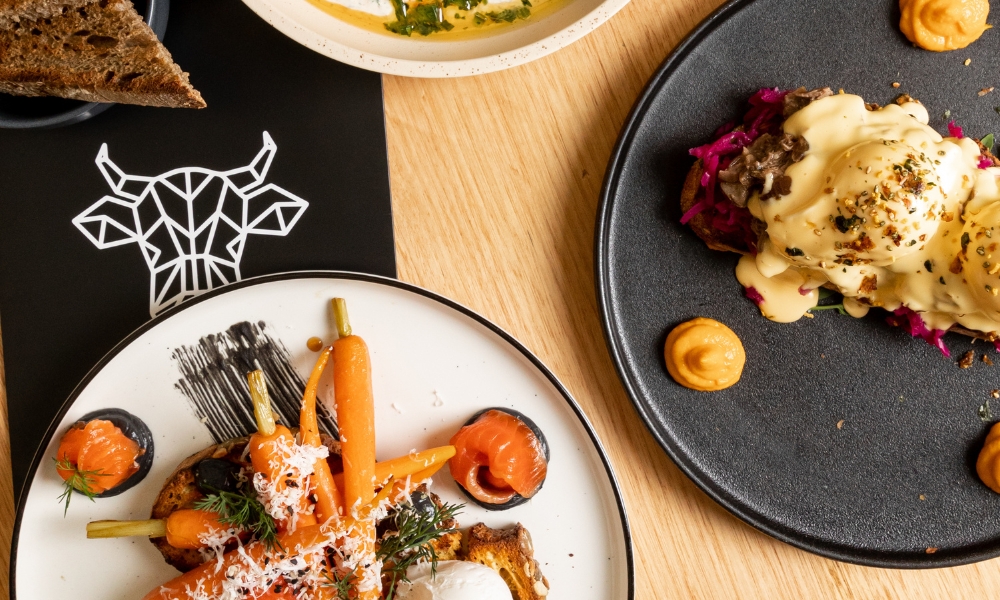 Two bright and colourful breakfast dishes sitting on a wooden table, with The Winey Cow menu.