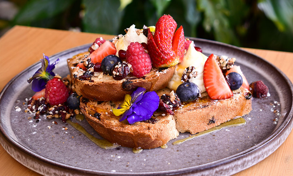 Plate of colorful french toast topped with fresh cream and a variety of different berries. garnished with colorful edible flowers.