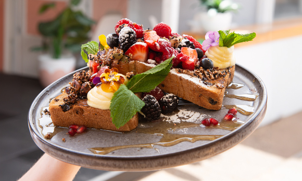 Plate of colorful french toast topped with fresh cream and a variety of different berries.