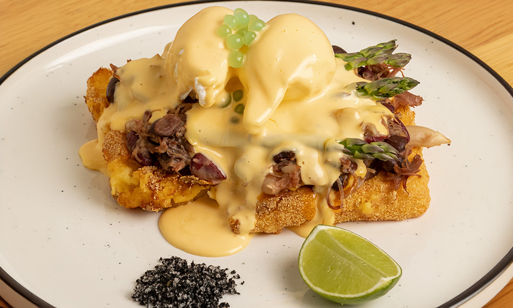 A beautiful plate of a breakfast meal featuring poached eggs and pulled beef topped with hollandaise sauce.