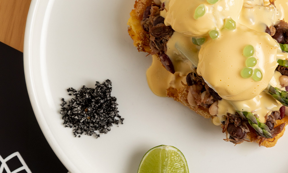 A close up top view perspective of a beautiful plate of a breakfast meal featuring poached eggs and pulled beef topped with hollandaise sauce.