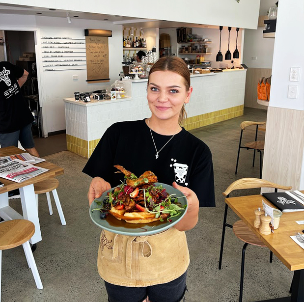 Smiling waitress at The Winey Cow holding a plate of deliciously presented food inside the bright and modern restaurant interior.