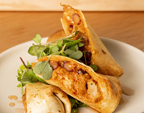 Savor the rich and savory flavors of The Winey Cow's stuffed tortilla, filled with a delectable mixture of beans, tender meat, and spices, wrapped in a golden, crisp shell and served with a fresh green garnish.