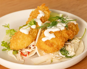 Indulge in our crispy fish tacos, featuring perfectly fried fish fillets, fresh slaw, and a drizzle of creamy sauce, garnished with herbs for a delightful taste experience at The Winey Cow.