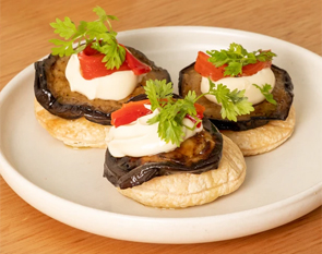 Savor our exquisite eggplant bites, layered with creamy topping and garnished with fresh herbs, perfect for a flavorful appetizer at The Winey Cow.