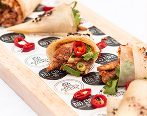 Flavorful chicken wrapped in soft crepes, garnished with fresh herbs and chili slices, offering a spicy and aromatic delight at The Winey Cow.