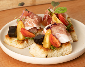 Savor the sophisticated flavors of prosciutto paired with heirloom tomatoes, served on crispy bread topped with fresh herbs at The Winey Cow.