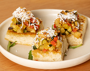 Freshly toasted focaccia topped with a colorful mix of sautéed vegetables and a sprinkle of cheese, providing a delightful and savory appetizer at The Winey Cow.