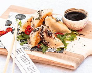 Golden pan-fried dumplings served with a tangy dipping sauce, providing a delightful and flavorful appetizer at The Winey Cow.