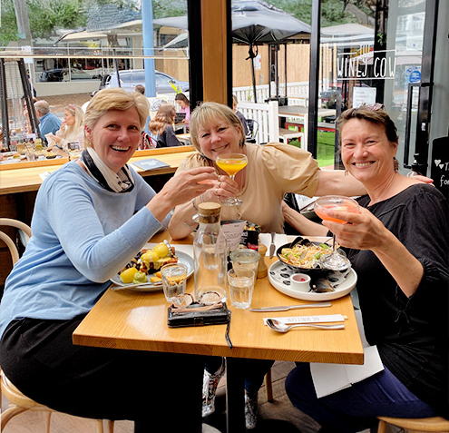 Group of three smiling ladies enjoying brunch as they cheers their mimosas.