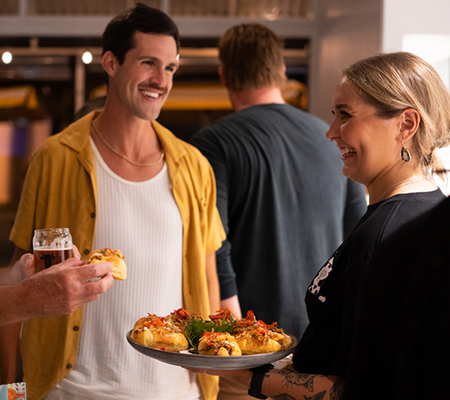 A smiling young woman serving catering appetizers to party guests.