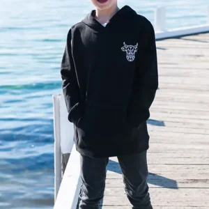 A young boy on a dock by the water wearing a black sweatshirt with The Winey Cow logo in white on the chest.