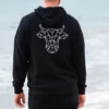 A man on the beach with his back facing the camera wearing a black sweatshirt with The Winey Cow logo in white on the back.