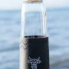 A glass water bottle with a bamboo top and a black silicone band around the bottom with The Winey Cow logo in white on the front.