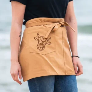 A tan apron with The Winey Cow logo in brown on the pocket.