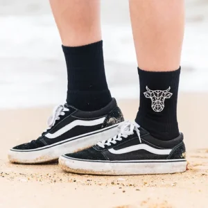 A young mans wearing black vans and black socks with The Winey Cow logo in white on the sides.