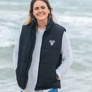 A smiling young woman wearing a puffer style vest with The Winey Cow logo in white on the chest.