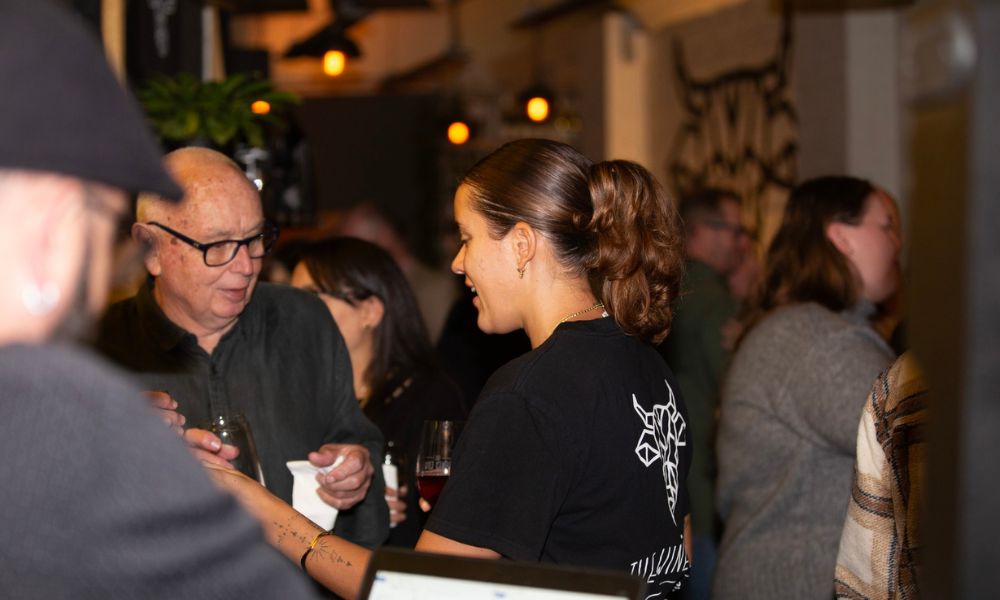 Photo of a staff member with a Winey Cow t'shirt interacting with a guest at a function held in their Mornington venue. The photo is dimly lit with ambient lighting.