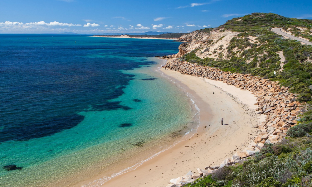 A Mornington Peninsula beach with blue and green waters, and cream sand.