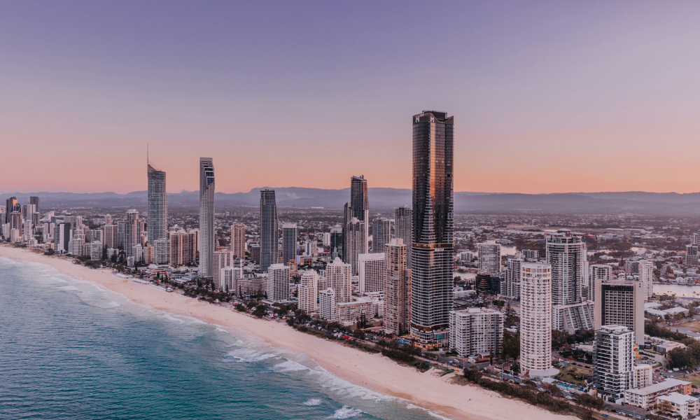 A photo where the buildings on the Gold Coast meet the sand and blue beached. It has a beautiful twilight sky